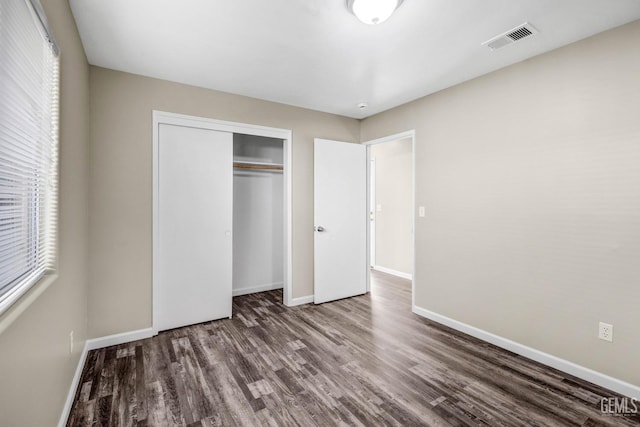 unfurnished bedroom featuring baseboards, multiple windows, visible vents, and wood finished floors