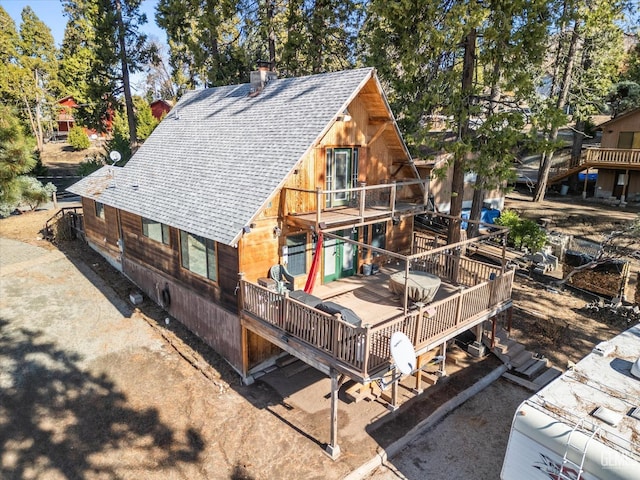 back of property featuring a wooden deck, a chimney, and roof with shingles