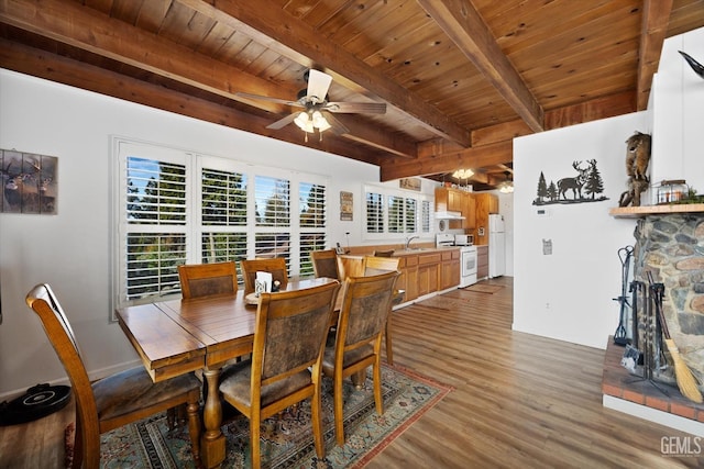 dining room featuring ceiling fan, a stone fireplace, wooden ceiling, wood finished floors, and beam ceiling