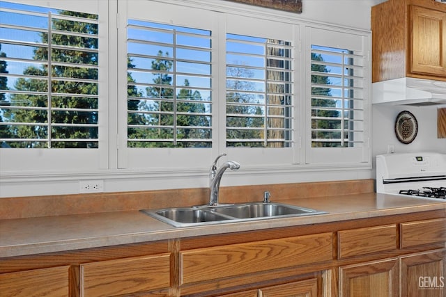 kitchen with gas range oven, light countertops, brown cabinetry, a sink, and under cabinet range hood