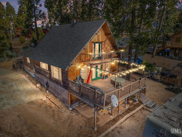 back of property at dusk featuring a chimney, roof with shingles, and a balcony