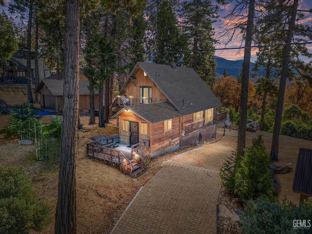 rear view of property featuring a deck, decorative driveway, and roof with shingles