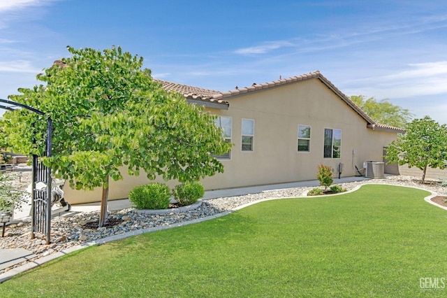 rear view of house featuring stucco siding, a yard, central AC, and a tile roof
