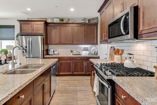 kitchen with tasteful backsplash, light stone countertops, light wood-type flooring, a sink, and stainless steel appliances