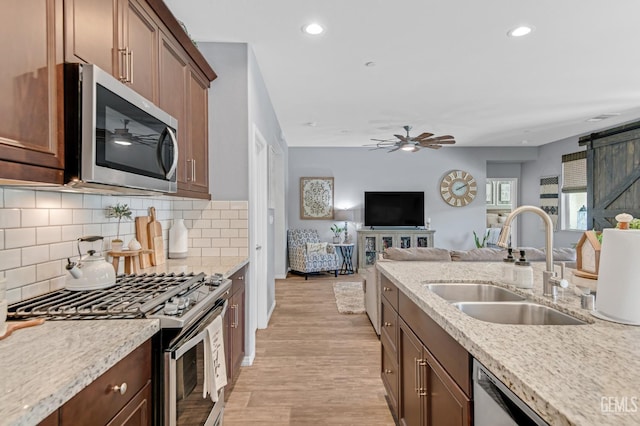 kitchen featuring ceiling fan, appliances with stainless steel finishes, a sink, open floor plan, and decorative backsplash