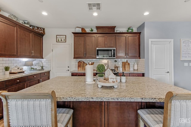 kitchen featuring backsplash, stainless steel microwave, a kitchen island, and visible vents