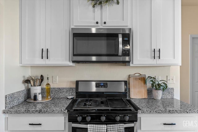 kitchen featuring light stone countertops, gas stove, and white cabinetry