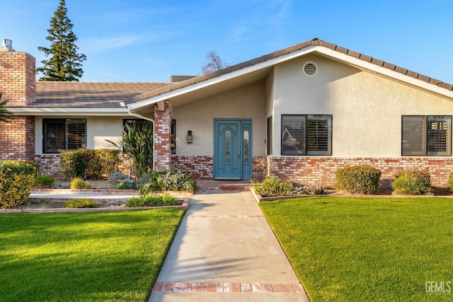 view of front facade featuring stucco siding, a front yard, and brick siding