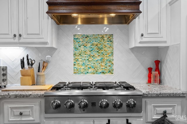 kitchen featuring stainless steel gas cooktop, custom exhaust hood, white cabinetry, and light stone countertops