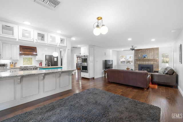 kitchen featuring glass insert cabinets, custom range hood, white cabinets, and hanging light fixtures