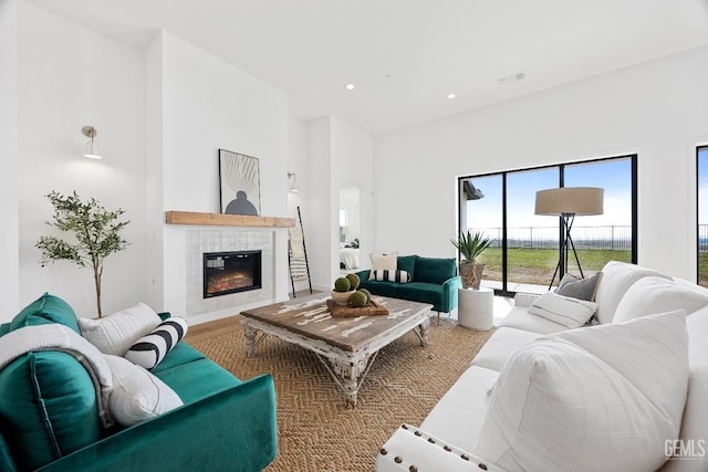 living area with recessed lighting, a towering ceiling, wood finished floors, visible vents, and a tiled fireplace