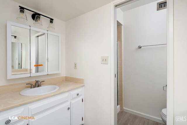 bathroom with hardwood / wood-style flooring, vanity, toilet, and a shower