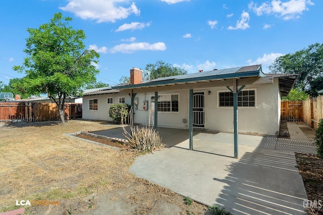2109 Custer Ave, Bakersfield, CA 93304 - back of property with stucco siding, a chimney, a fenced backyard, a patio, and roof mounted solar panels