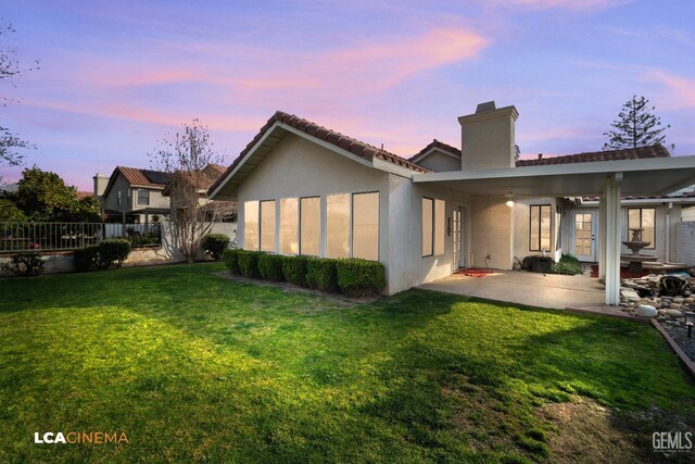 back house at dusk featuring a patio and a lawn