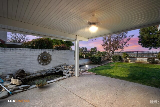 patio terrace at dusk featuring ceiling fan and a lawn