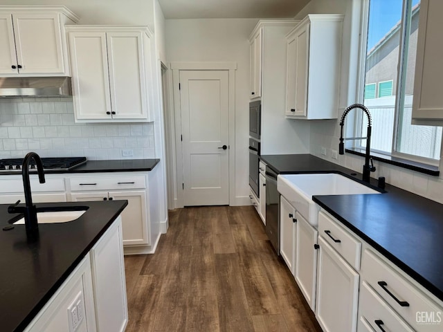 kitchen with dark countertops, white cabinets, under cabinet range hood, and dark wood-style floors