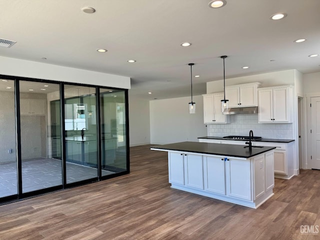 kitchen featuring dark countertops, white cabinetry, wood finished floors, under cabinet range hood, and visible vents