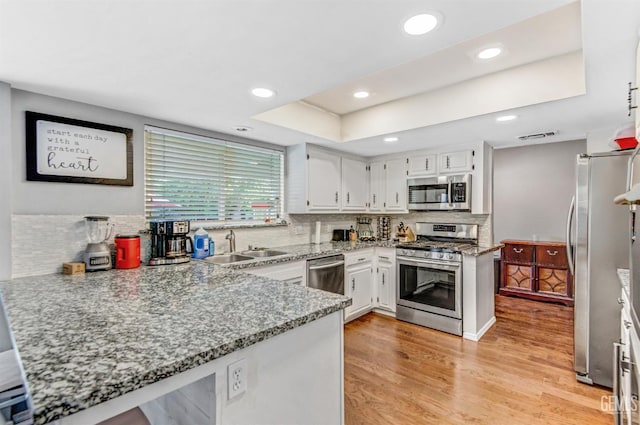 7701 Shetland Dr, Bakersfield, CA 93309 - kitchen with appliances with stainless steel finishes, tasteful backsplash, white cabinets, light wood-style floors, and a peninsula