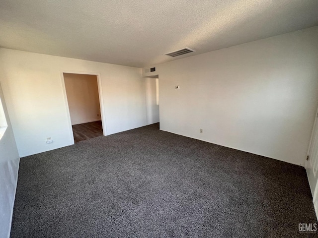 spare room with a textured ceiling and dark carpet