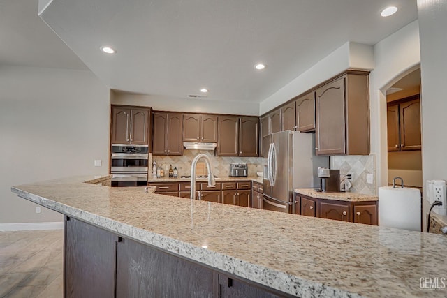 kitchen with under cabinet range hood, decorative backsplash, recessed lighting, appliances with stainless steel finishes, and arched walkways