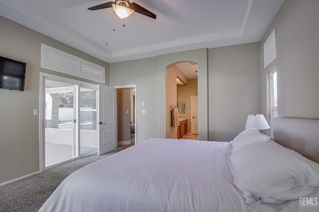 carpeted bedroom featuring connected bathroom, arched walkways, a raised ceiling, and access to outside