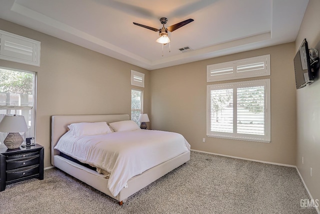 bedroom with visible vents, baseboards, light carpet, a raised ceiling, and a ceiling fan