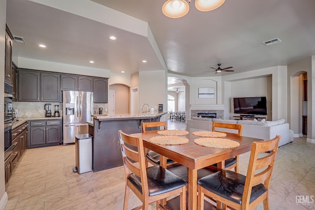 dining space with visible vents, a brick fireplace, a ceiling fan, and arched walkways