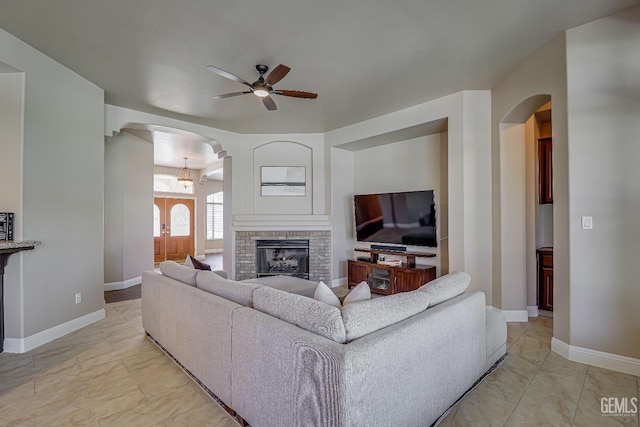 living room with a brick fireplace, a ceiling fan, arched walkways, and baseboards