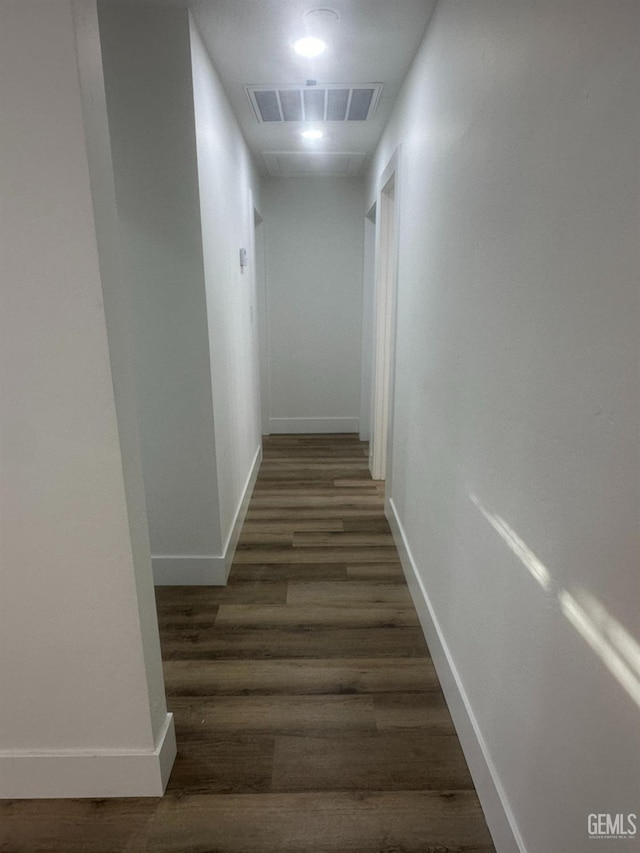 hallway with baseboards, visible vents, and wood finished floors