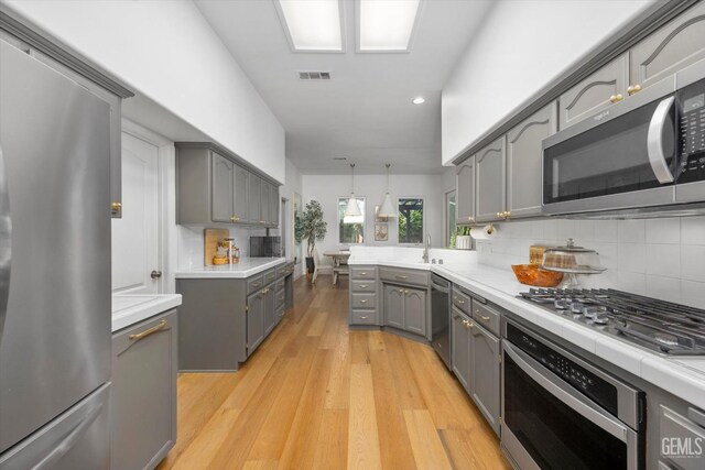 6707 Park W Cir, Bakersfield, CA 93308 - kitchen with gray cabinetry, appliances with stainless steel finishes, a peninsula, backsplash, and light wood finished floors