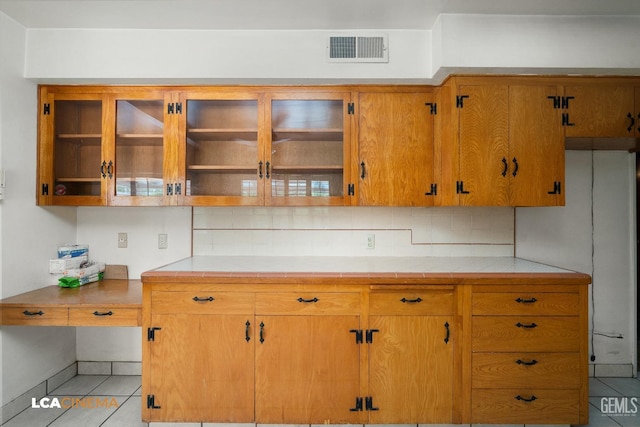 kitchen with light tile patterned floors, decorative backsplash, visible vents, glass insert cabinets, and brown cabinets