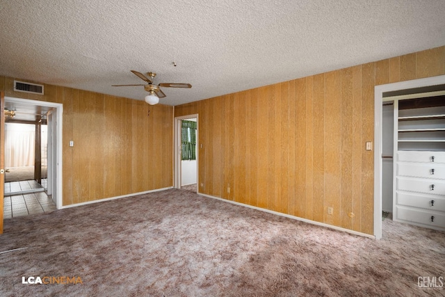 unfurnished bedroom featuring carpet, a textured ceiling, wooden walls, visible vents, and a closet