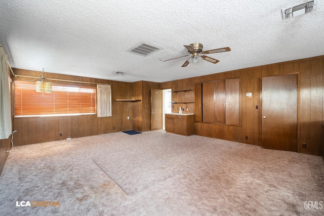 unfurnished living room with visible vents, wooden walls, and a ceiling fan