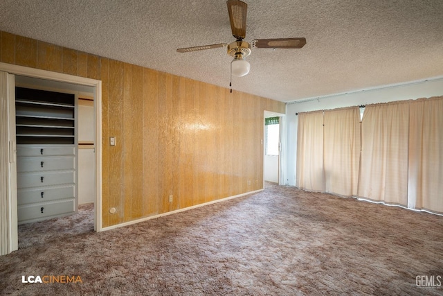 unfurnished bedroom featuring ceiling fan, wood walls, carpet flooring, and a textured ceiling
