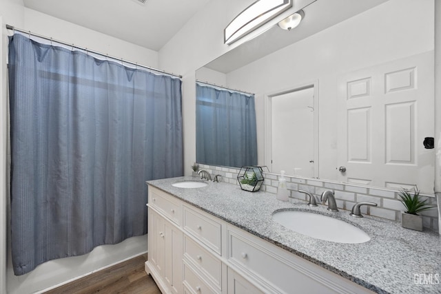 bathroom featuring wood finished floors, a sink, decorative backsplash, and double vanity