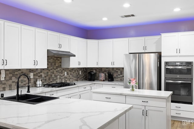 kitchen with black gas cooktop, under cabinet range hood, a sink, backsplash, and freestanding refrigerator