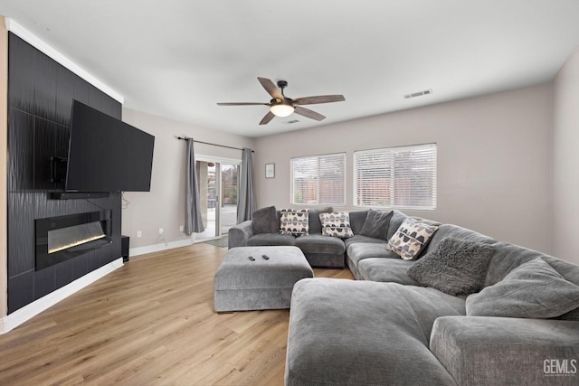 living area featuring a fireplace, visible vents, baseboards, a ceiling fan, and light wood-type flooring