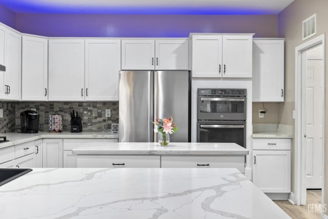 kitchen featuring visible vents, white cabinetry, freestanding refrigerator, light stone countertops, and multiple ovens