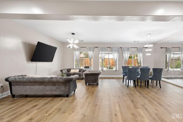 living room with a chandelier, light wood-type flooring, baseboards, and a healthy amount of sunlight