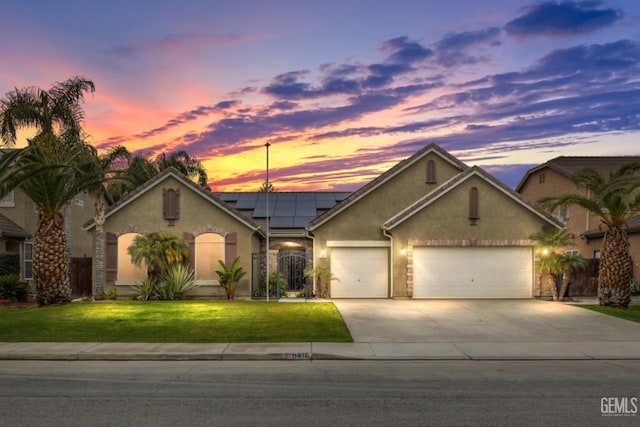 view of front of home featuring a garage, driveway, solar panels, a front lawn, and stucco siding