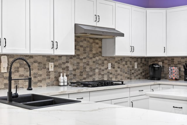 kitchen featuring black gas stovetop, under cabinet range hood, a sink, white cabinetry, and light stone countertops