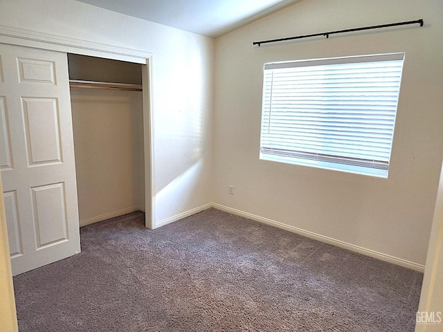 unfurnished bedroom with dark colored carpet, lofted ceiling, and a closet