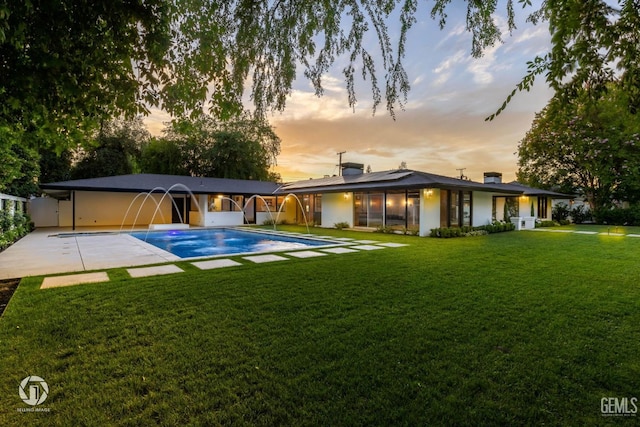 2221 Myrtle St, Bakersfield, CA 93301 - back of house at dusk with a lawn, roof mounted solar panels, an outdoor pool, a chimney, and a patio area