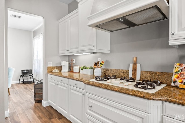 kitchen featuring white gas stovetop, visible vents, white cabinets, wood finished floors, and ventilation hood