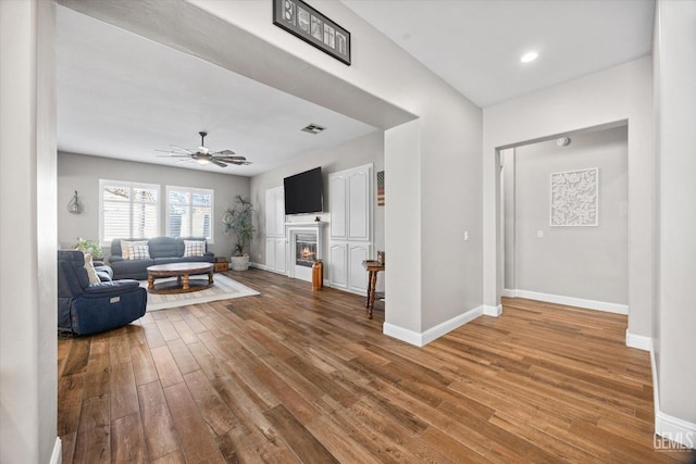 living area with visible vents, hardwood / wood-style floors, a ceiling fan, a glass covered fireplace, and baseboards