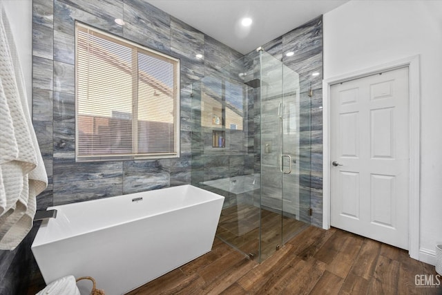 bathroom with a shower stall, a freestanding bath, tile walls, and wood finished floors