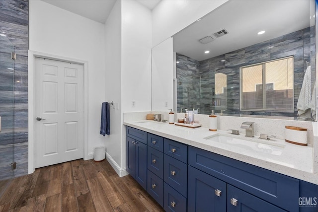 full bathroom with double vanity, a shower stall, a sink, and wood finished floors