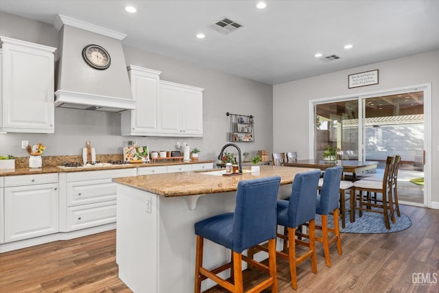 kitchen with custom range hood, a sink, visible vents, and wood finished floors