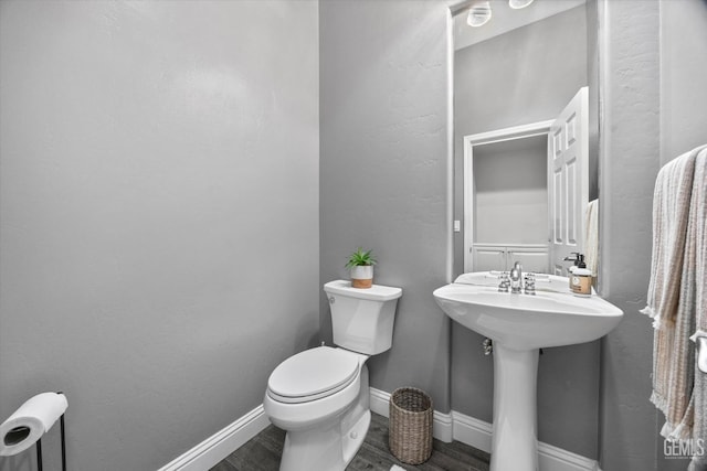 half bathroom featuring a sink, toilet, baseboards, and wood finished floors