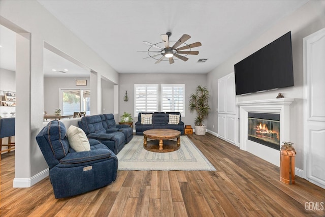 living area featuring a glass covered fireplace, wood finished floors, visible vents, and baseboards